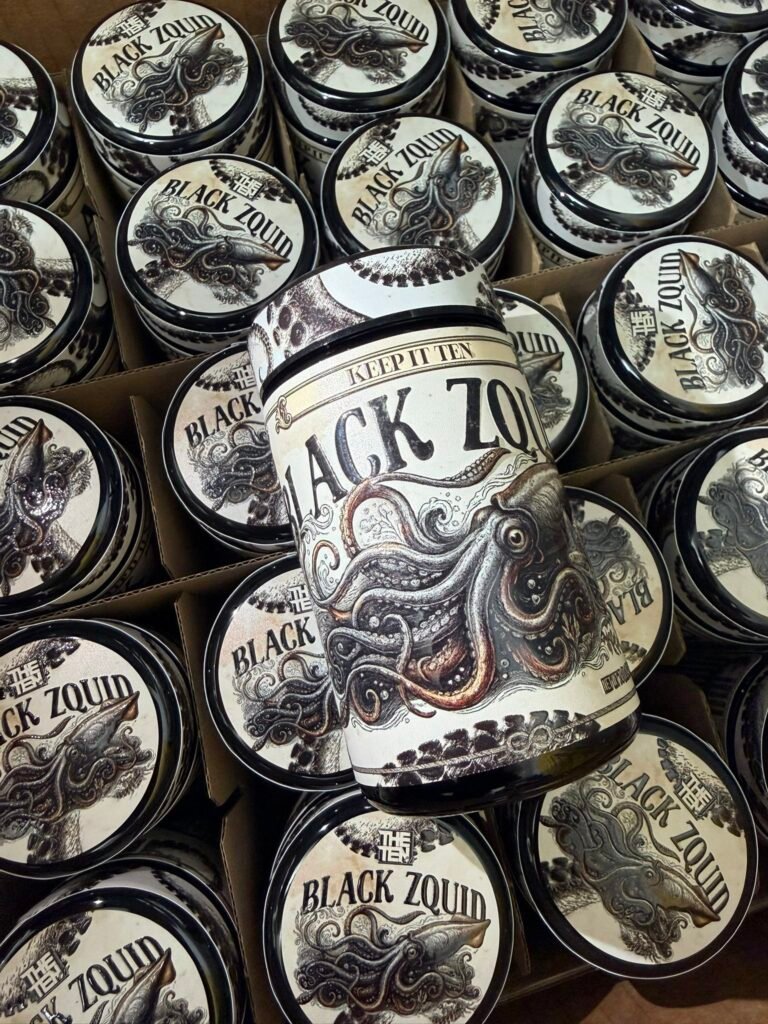 Close-up of multiple round tins with a black-and-white label that reads 'BLACK ZQUID' and features an octopus illustration in a boxful display.