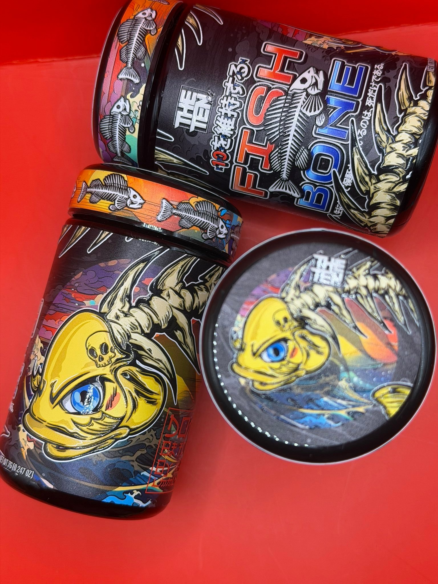 Close-up of decorated metal cans with colorful dragon and skull artwork on black backgrounds against a red backdrop.