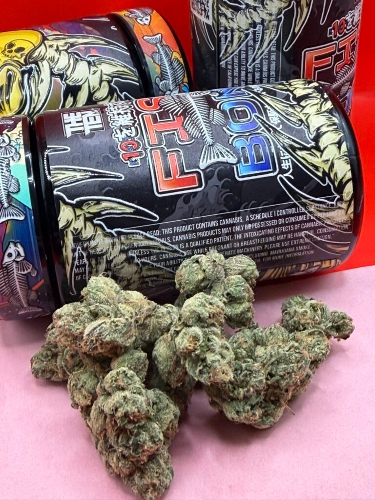 Close-up of cannabis buds in front of a black, graphic-printed container with red lettering in the background.