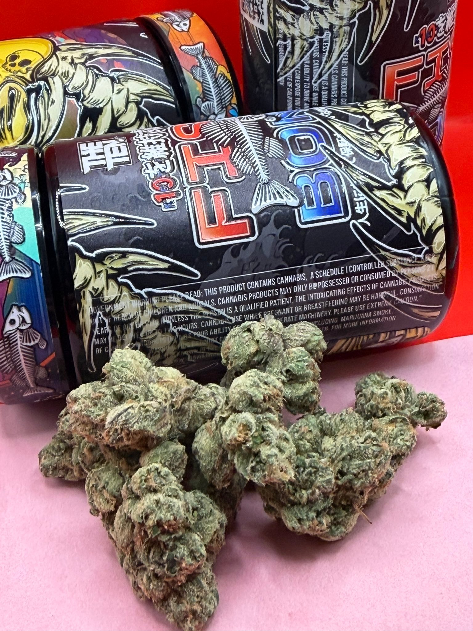 Close-up of cannabis buds in front of a black, graphic-printed container with red lettering in the background.