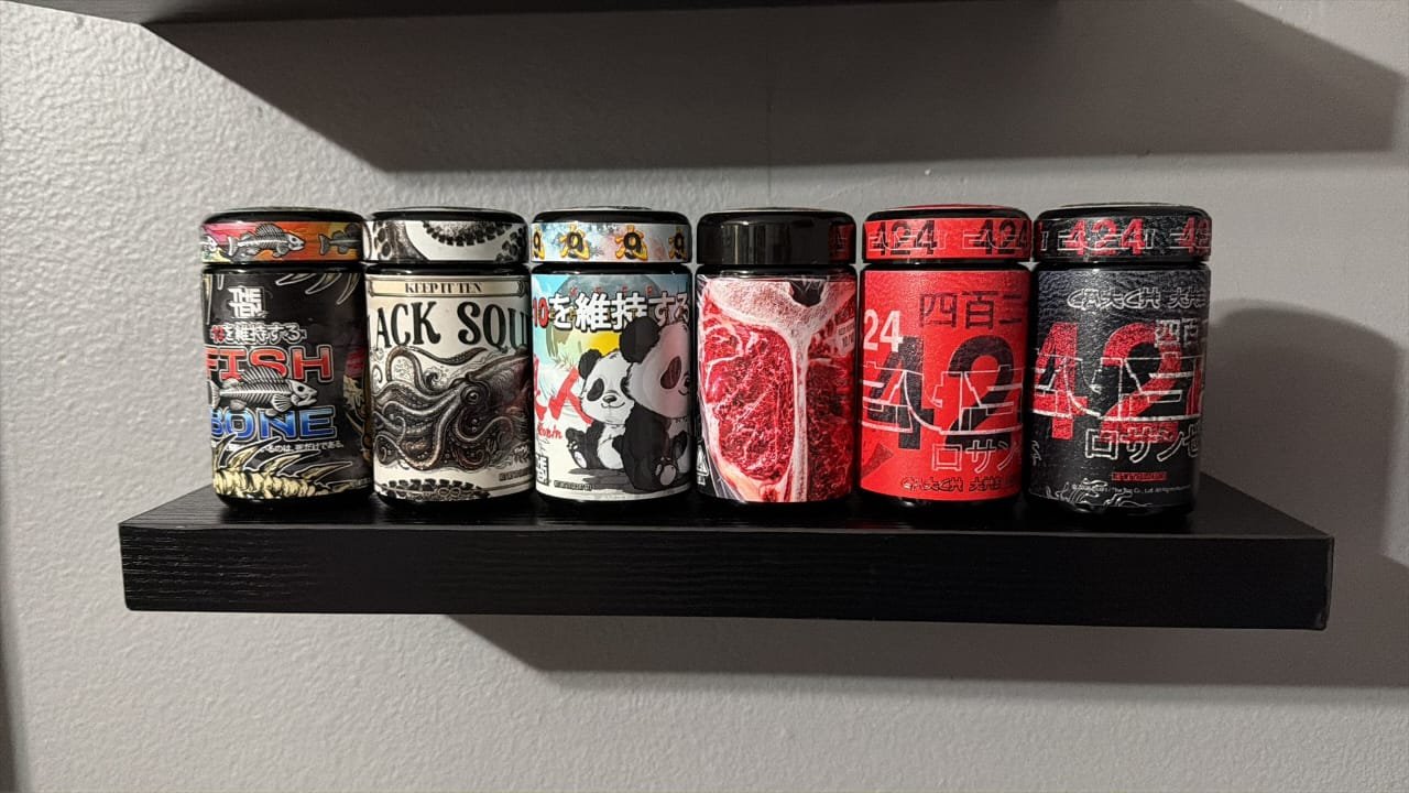 Six novelty jars with bold, graphic labels lined up on a black wall shelf.