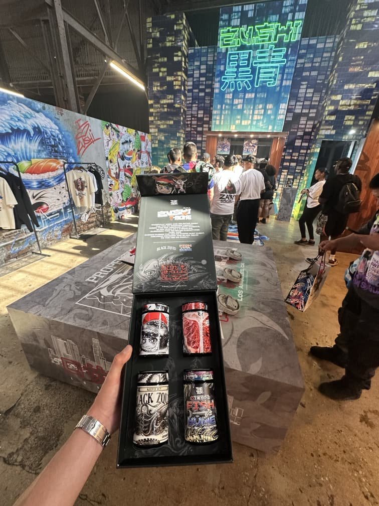 Hand holding Zalympix 2026 Zushi strain gift box with Black Zoid, Fish & Bone, and other premium cannabis jars at THE TENCO booth
